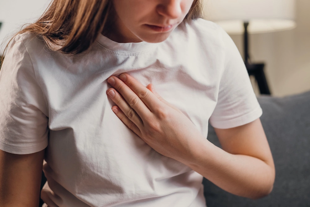 Young unhealthy female sit on couch having difficulty breathing pain of heart