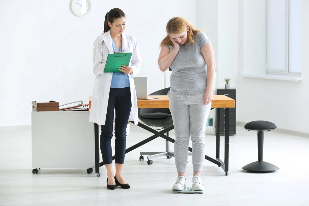 Young female doctor measuring weight of overweight woman in clinic