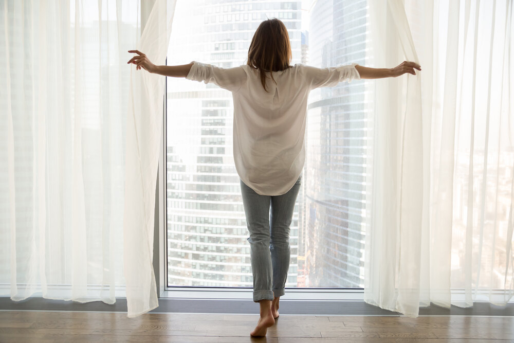 Rear view at woman standing looking out of full-length window of luxury modern apartment