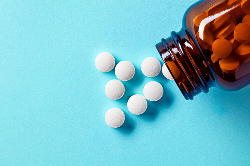 White medical pills and tablets spilling out of a drug bottle.