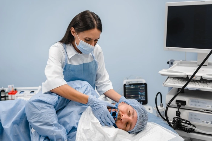 Man male patient laying at the bed while assistant holding special equipment at his mouth