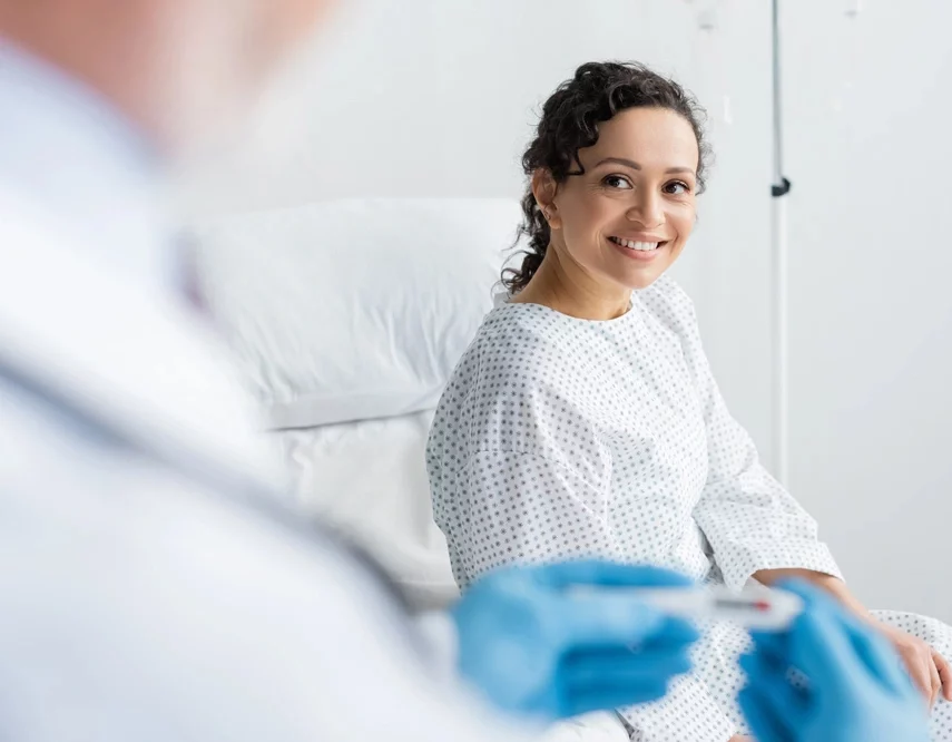 woman smiling near doctor in latex gloves holding thermometer on blurred foreground