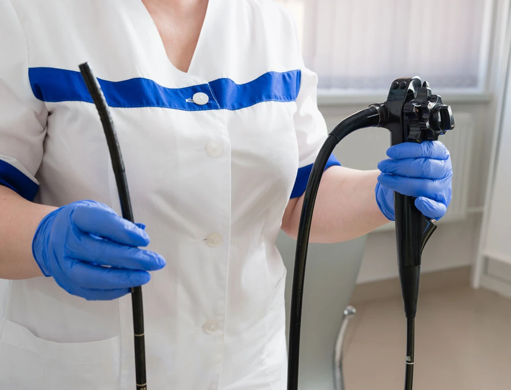 A female doctor in a white suit holds medical equipment for video esophagogastroduodenoscopy in her hands in blue gloves