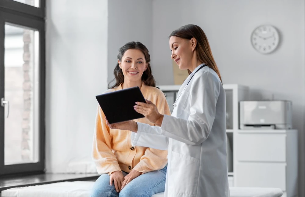 female doctor with tablet pc computer talking to smiling woman patient at hospital