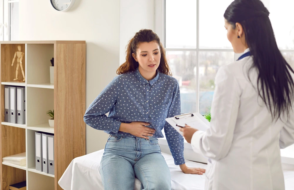 Female medical specialist consults young female patient who complains of abdominal pain.
