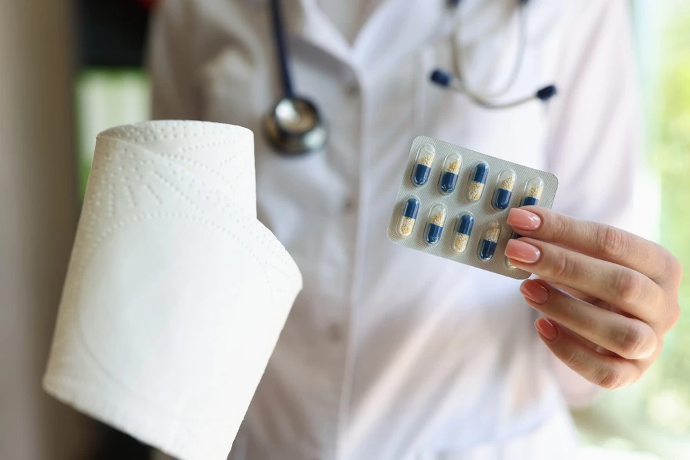 Doctor is holding roll of toilet paper and pack of capsules close-up.