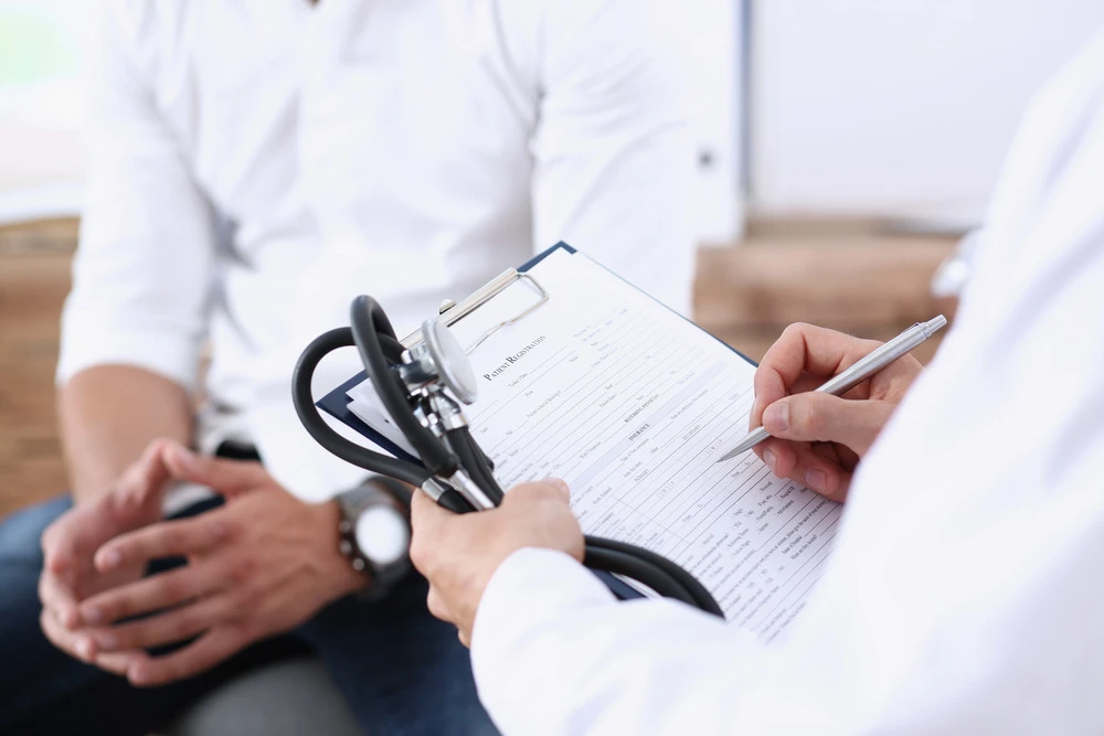 Male doctor hand hold silver pen filling patient history list at clipboard pad