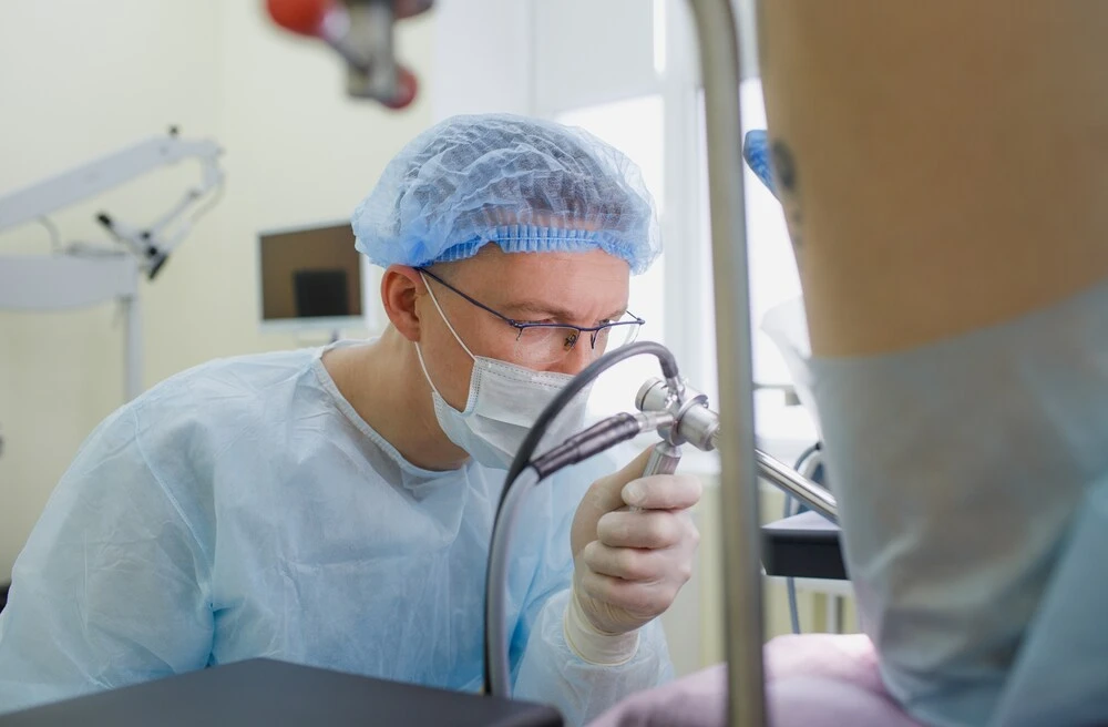 a proctologist examines a rectal colonoscopy patient lying on a medical chair in the surgical office