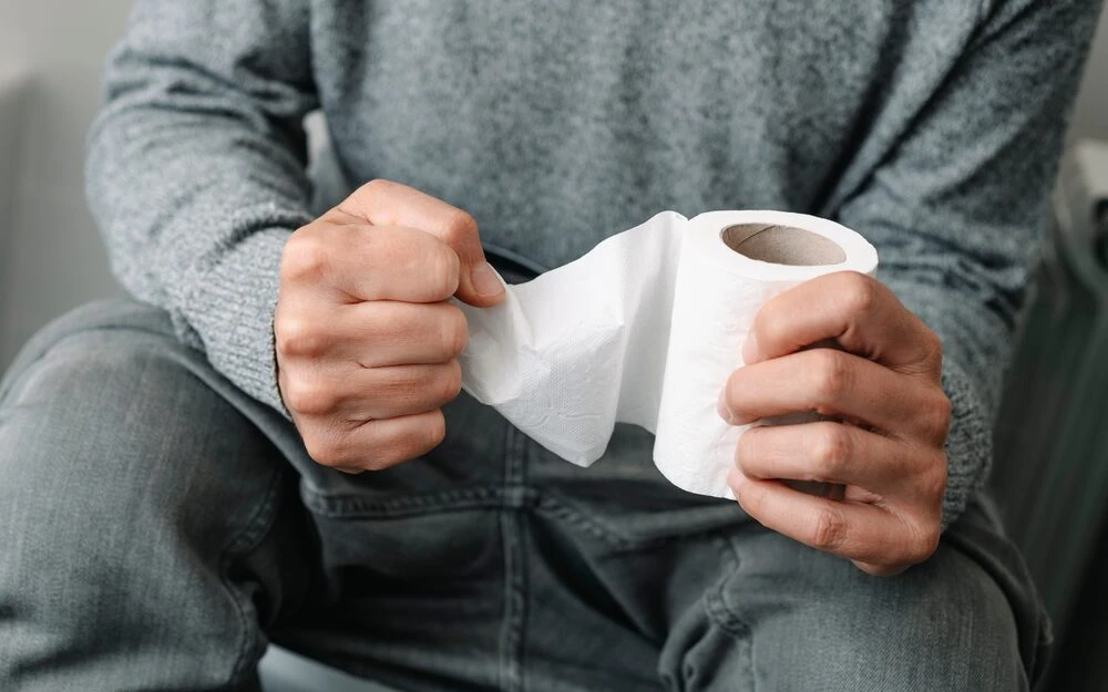 a caucasian man, sitting in the toilet, grabs tight the toilet paper