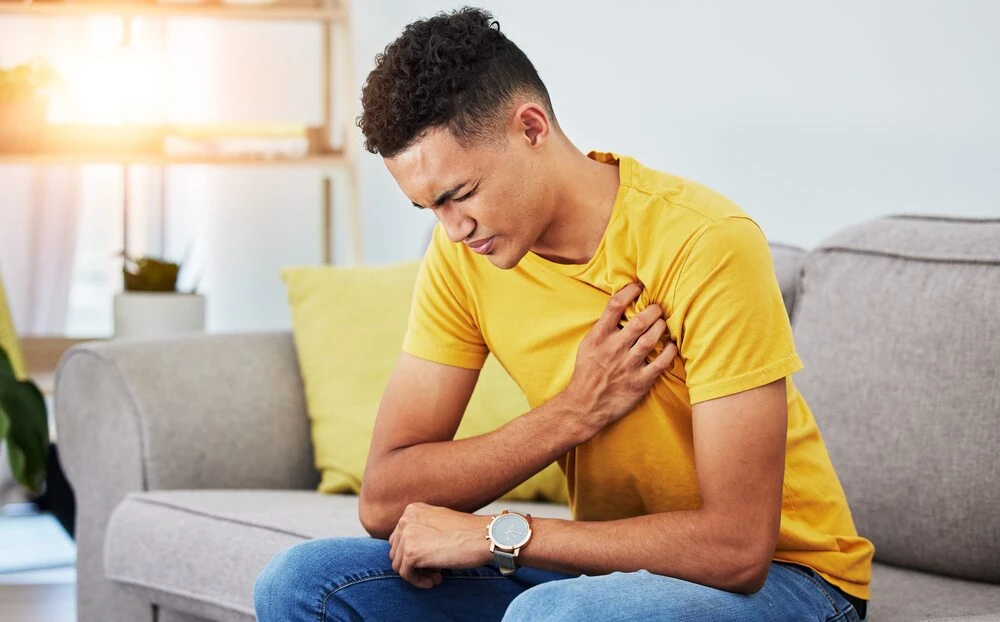 Man, sofa and chest pain in home, massage and relief from stress or injury in living room.